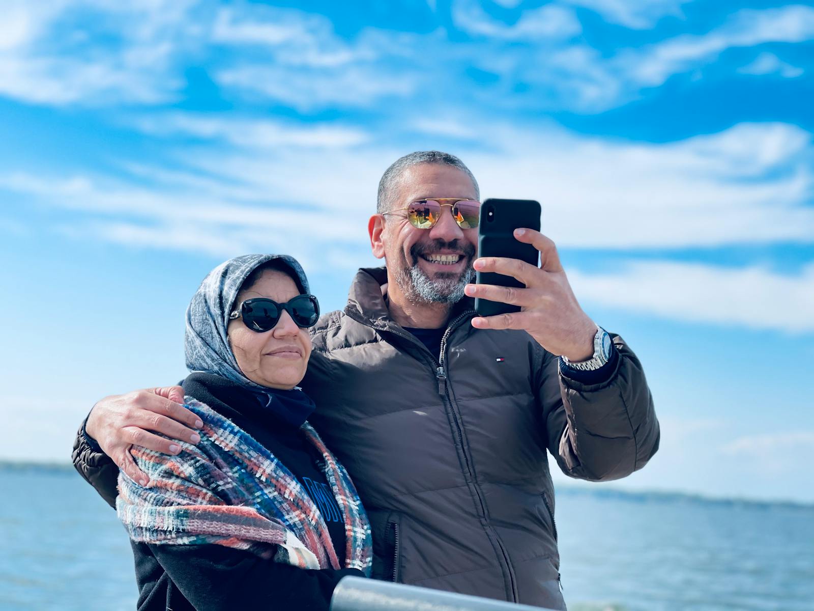 Couple enjoying a sunny day by the sea, capturing memories with a selfie.